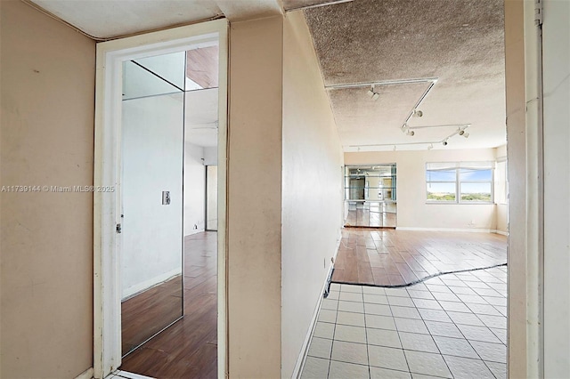 hallway with baseboards, rail lighting, and light tile patterned floors