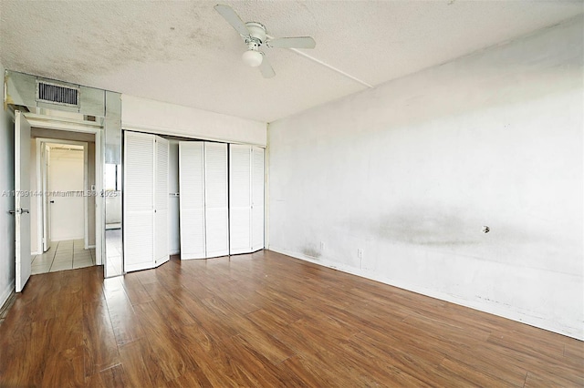 unfurnished bedroom featuring wood finished floors, a closet, a ceiling fan, baseboards, and a textured ceiling