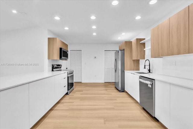 kitchen featuring appliances with stainless steel finishes, sink, white cabinets, light brown cabinets, and light hardwood / wood-style flooring