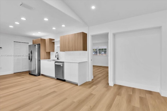 kitchen with appliances with stainless steel finishes, sink, white cabinets, and light hardwood / wood-style floors