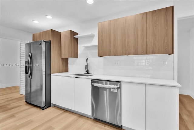 kitchen featuring appliances with stainless steel finishes, sink, light hardwood / wood-style flooring, and white cabinets