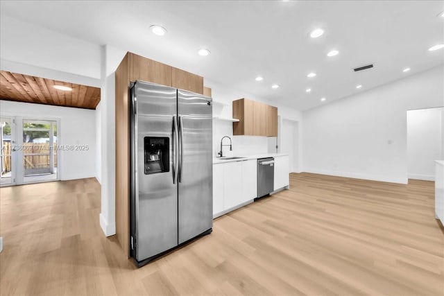 kitchen featuring sink, appliances with stainless steel finishes, white cabinets, vaulted ceiling, and light wood-type flooring