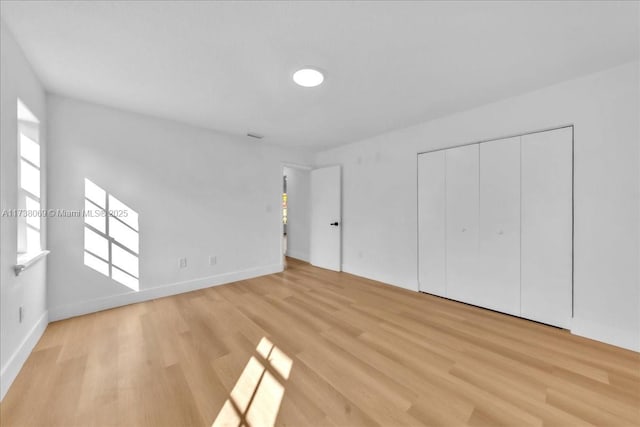 unfurnished bedroom featuring multiple windows, light hardwood / wood-style floors, and a closet