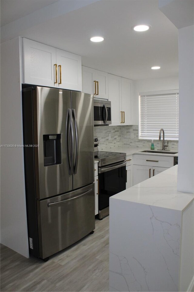 kitchen with sink, appliances with stainless steel finishes, light stone countertops, white cabinets, and decorative backsplash