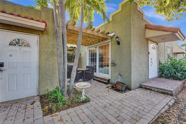 view of exterior entry featuring stucco siding, a patio, and a pergola