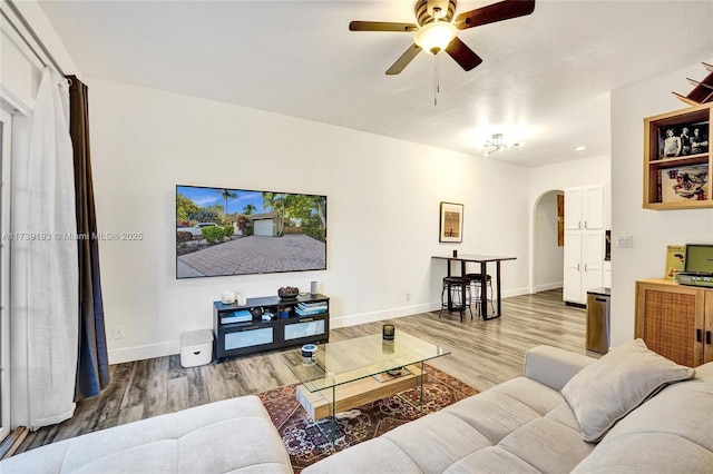 living area with arched walkways, wood finished floors, a ceiling fan, and baseboards