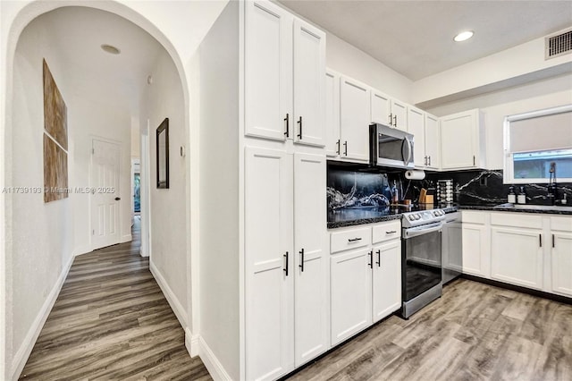 kitchen with light wood finished floors, arched walkways, a sink, stainless steel appliances, and dark countertops