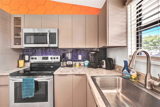 kitchen featuring light stone counters, appliances with stainless steel finishes, sink, and backsplash