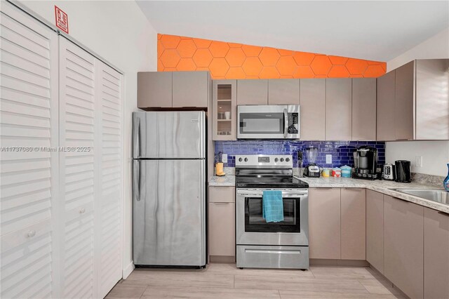 kitchen featuring sink, gray cabinets, stainless steel appliances, light stone countertops, and decorative backsplash