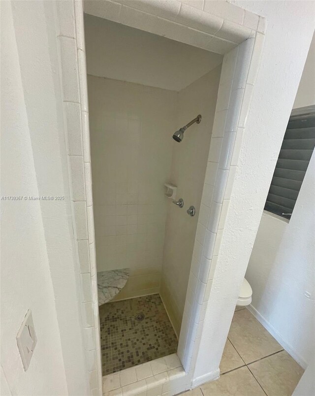 bathroom with tile patterned flooring, a tile shower, and toilet