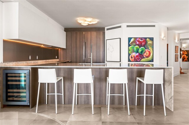 kitchen featuring wine cooler, a kitchen breakfast bar, and white cabinets