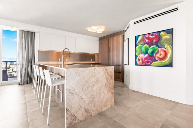 kitchen with a breakfast bar area, sink, a center island with sink, and white cabinets