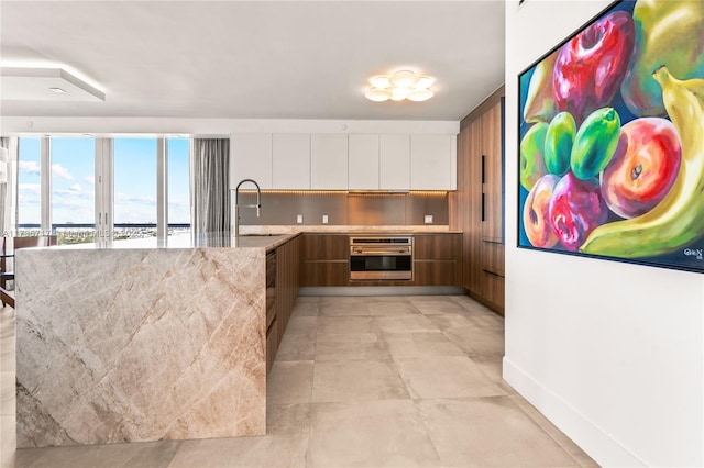 kitchen with white cabinetry, oven, sink, and light stone countertops