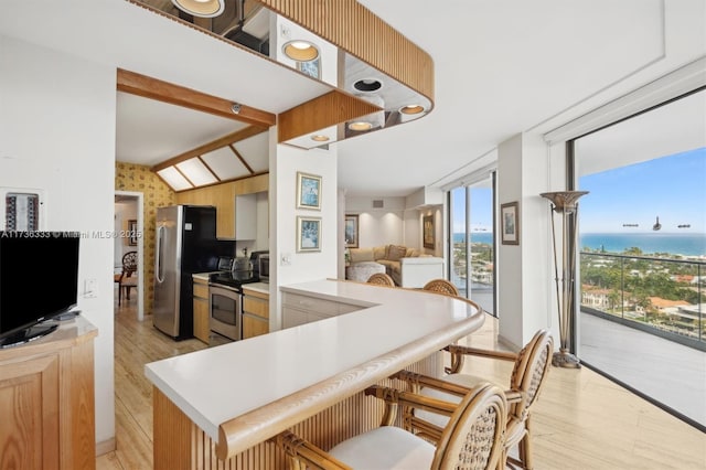 kitchen with appliances with stainless steel finishes, a water view, lofted ceiling with beams, expansive windows, and kitchen peninsula