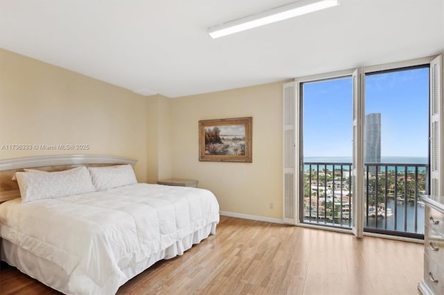 bedroom featuring a water view, a wall of windows, and light hardwood / wood-style floors