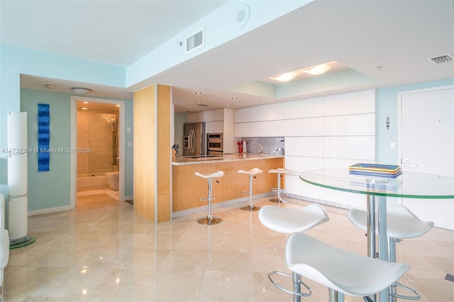 kitchen with white cabinetry, stainless steel appliances, a kitchen breakfast bar, decorative backsplash, and kitchen peninsula