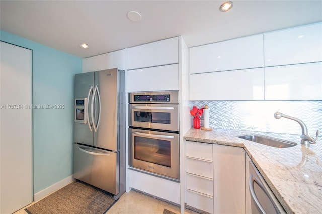 kitchen with sink, stainless steel appliances, light stone counters, white cabinets, and decorative backsplash