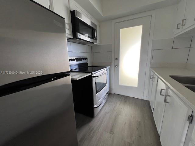 kitchen with stainless steel appliances, white cabinets, light wood-type flooring, and decorative backsplash