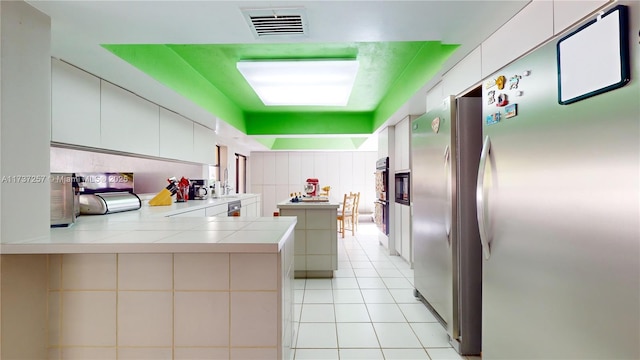 kitchen featuring light tile patterned flooring, white cabinets, stainless steel refrigerator, and kitchen peninsula