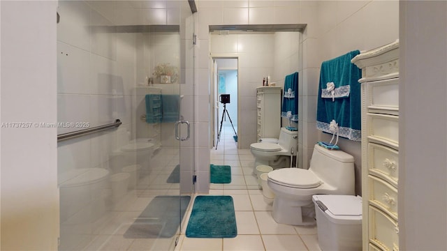 bathroom with tile walls, tile patterned flooring, toilet, a shower with door, and a bidet