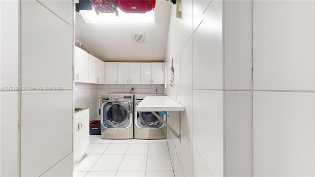 clothes washing area with cabinets, washing machine and dryer, light tile patterned floors, and tile walls