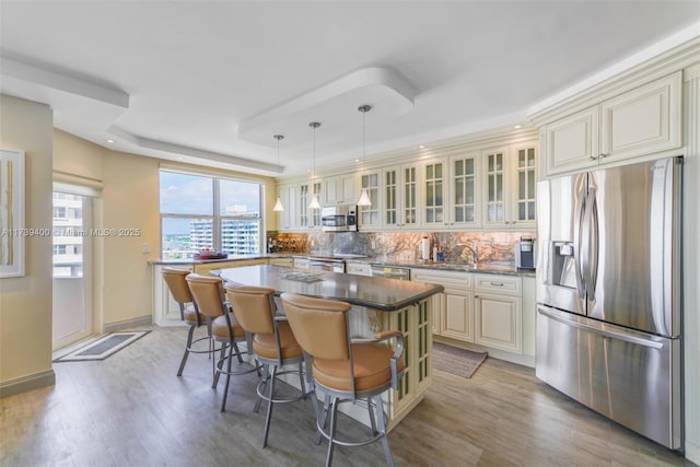 kitchen with a kitchen island, appliances with stainless steel finishes, backsplash, hanging light fixtures, and cream cabinets