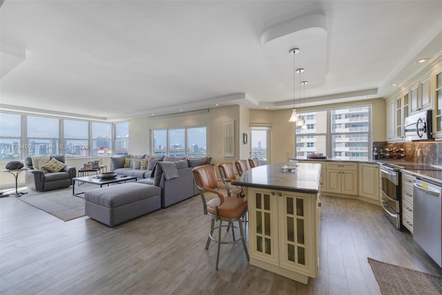 kitchen with appliances with stainless steel finishes, decorative light fixtures, a center island, cream cabinets, and light hardwood / wood-style flooring