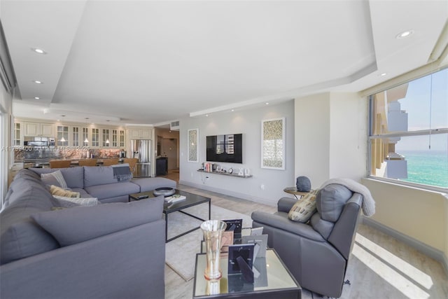 living room with a water view, a raised ceiling, and light hardwood / wood-style floors