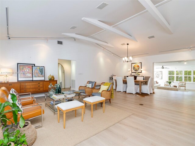 living room with ceiling fan with notable chandelier, track lighting, light hardwood / wood-style floors, and lofted ceiling with beams