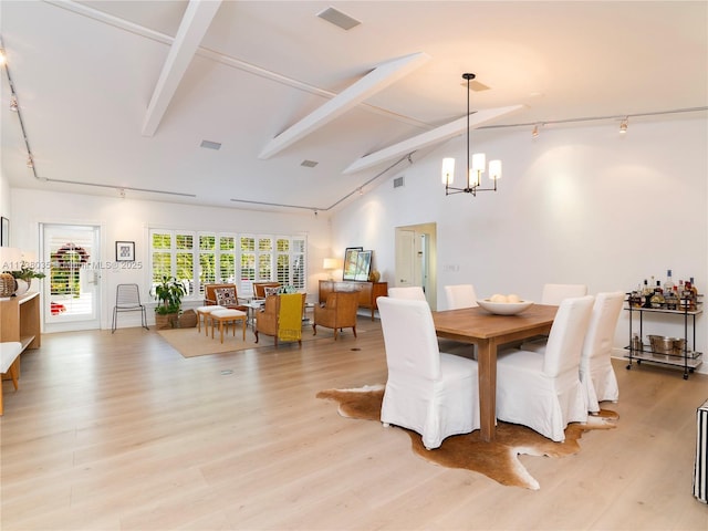 dining space with light hardwood / wood-style flooring, an inviting chandelier, beam ceiling, high vaulted ceiling, and track lighting