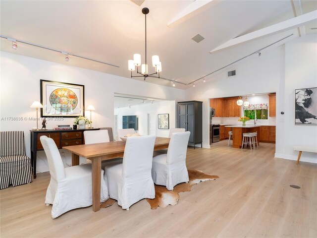 dining space with high vaulted ceiling, a chandelier, light hardwood / wood-style floors, track lighting, and beam ceiling