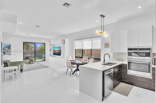 kitchen featuring sink, white cabinets, decorative backsplash, hanging light fixtures, and stainless steel appliances