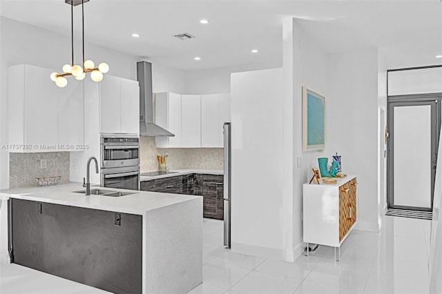 kitchen with appliances with stainless steel finishes, decorative light fixtures, sink, white cabinets, and wall chimney exhaust hood