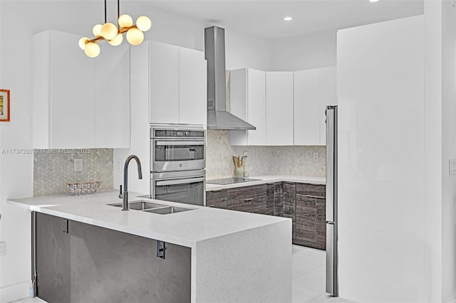 kitchen with appliances with stainless steel finishes, white cabinets, decorative light fixtures, kitchen peninsula, and wall chimney exhaust hood