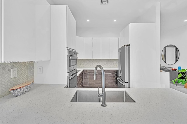 kitchen with sink, tasteful backsplash, stainless steel appliances, light stone countertops, and white cabinets