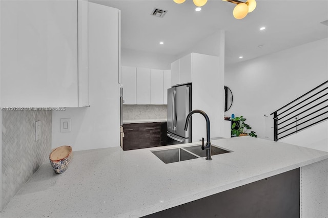 kitchen featuring sink, stainless steel refrigerator, white cabinetry, backsplash, and kitchen peninsula