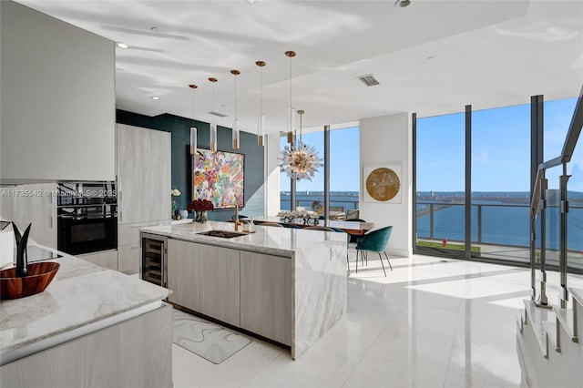 kitchen featuring decorative light fixtures, sink, light stone counters, a water view, and a center island with sink