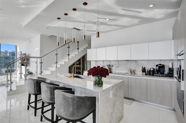 kitchen with white cabinetry, hanging light fixtures, decorative backsplash, and a large island with sink