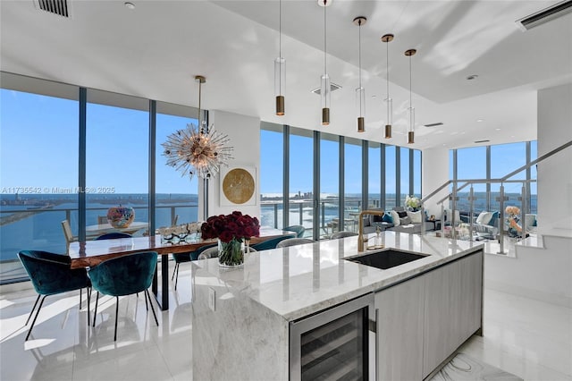 kitchen with pendant lighting, light stone counters, beverage cooler, and a water view