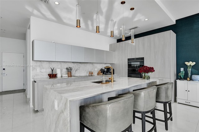 kitchen featuring a breakfast bar, an island with sink, sink, hanging light fixtures, and black appliances