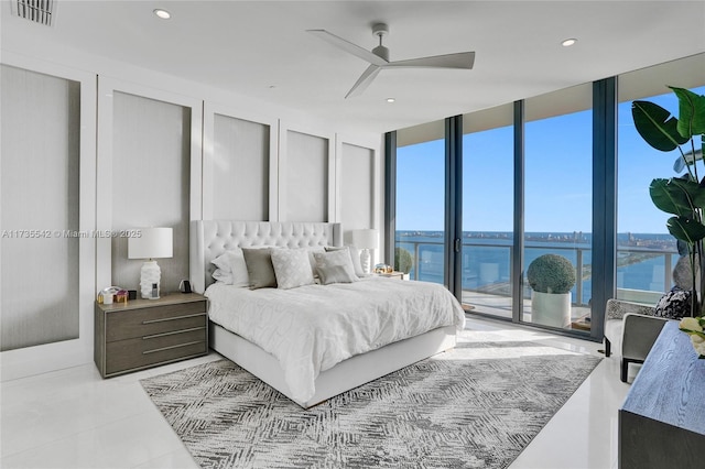 bedroom with access to exterior, expansive windows, ceiling fan, and a water view