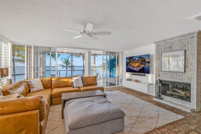 living room featuring ceiling fan, a large fireplace, a healthy amount of sunlight, and a textured ceiling