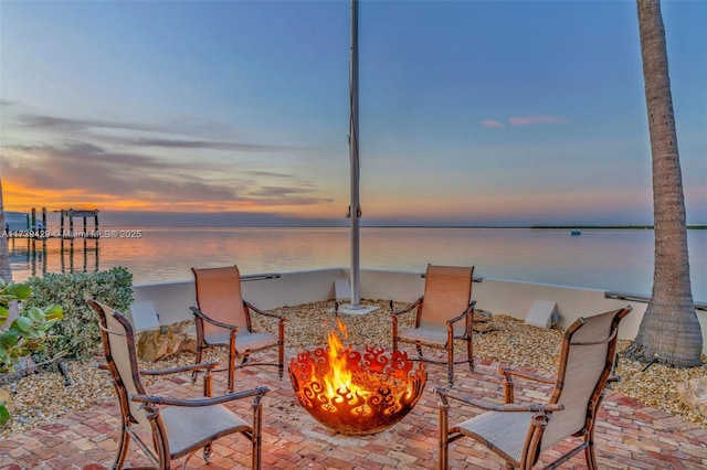 patio terrace at dusk with a water view and an outdoor fire pit