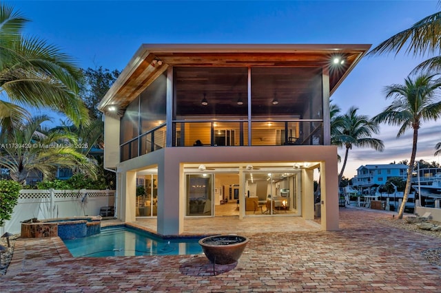 back house at dusk with a balcony, a pool with hot tub, and a patio area