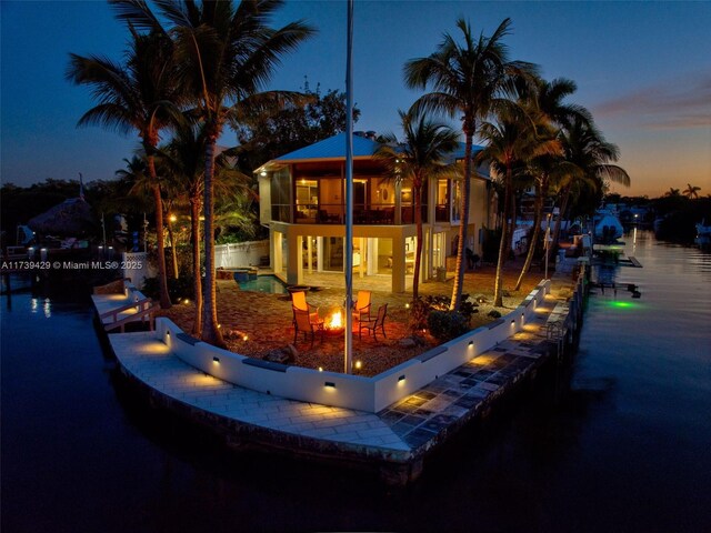 back house at dusk with a balcony, a water view, and a patio area