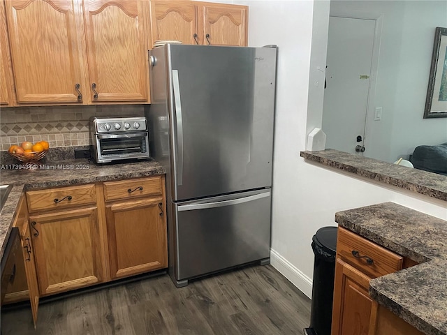 kitchen featuring backsplash, dark wood-type flooring, stainless steel fridge, and black dishwasher