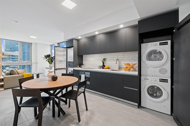 kitchen with sink, light tile patterned floors, stacked washing maching and dryer, backsplash, and stainless steel appliances