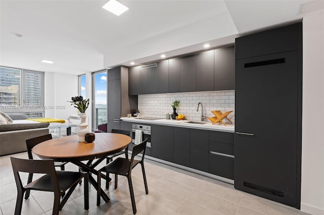 kitchen with light tile patterned floors, sink, backsplash, black electric cooktop, and stainless steel oven