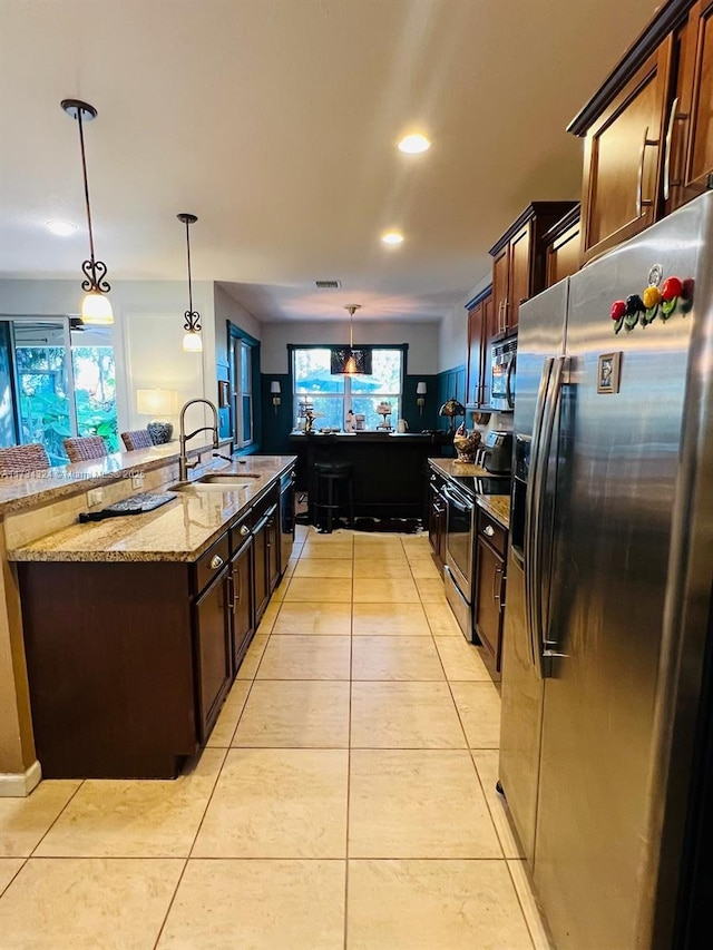 kitchen featuring pendant lighting, sink, stainless steel appliances, light stone counters, and dark brown cabinetry