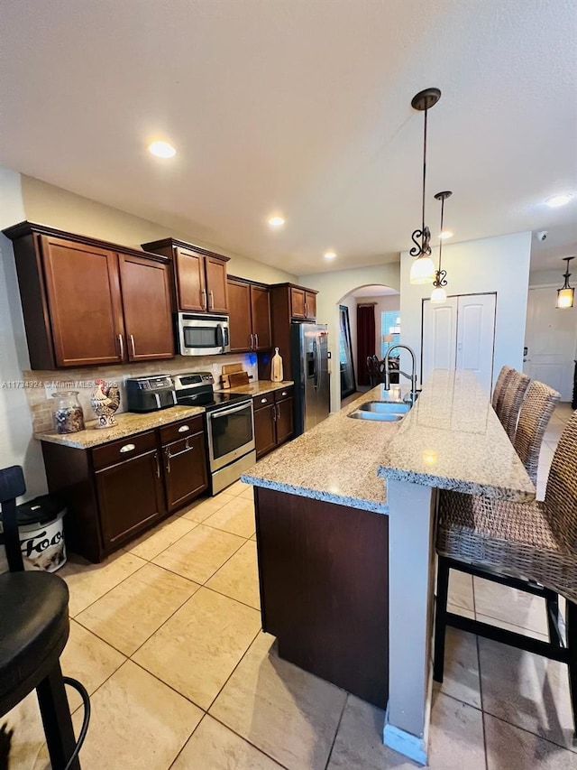 kitchen with sink, a breakfast bar, hanging light fixtures, stainless steel appliances, and an island with sink